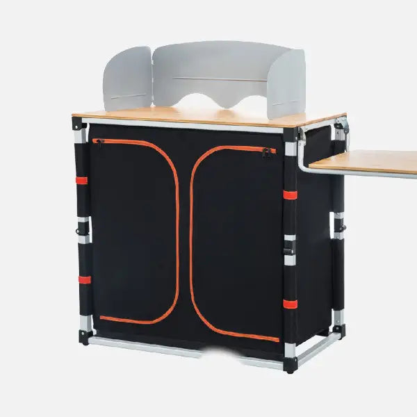 Zur Kategorie Campingschränke: Zusammenklappbare Outdoor-Küchenbox mit Arbeitsplatte, Windschutz und schwarzen Staufächern mit orangefarbener Umrandung.
